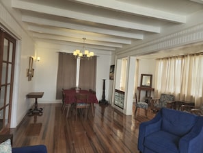 Un coin repas avec une table dressée pour quatre personnes, un lustre et une vue sur l’extérieur à travers une fenêtre ornée de rideaux.