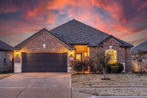 A residential house with a brick exterior, a dark garage door, and a well-lit front entrance. - Crowley | Insurance & Crew Ready · Office · Yard (Crowley)