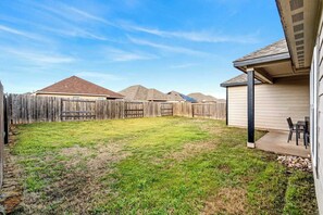 A backyard with a wooden fence, a grassy lawn, and a covered patio area with a table and chairs. - Crowley | Insurance & Crew Ready · Office · Yard (Crowley)