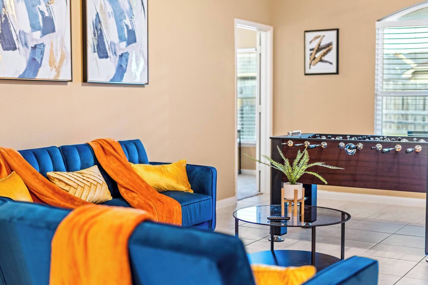 Una sala de estar moderna con un sofá azul, un cojín naranja y una mesa de centro de vidrio.