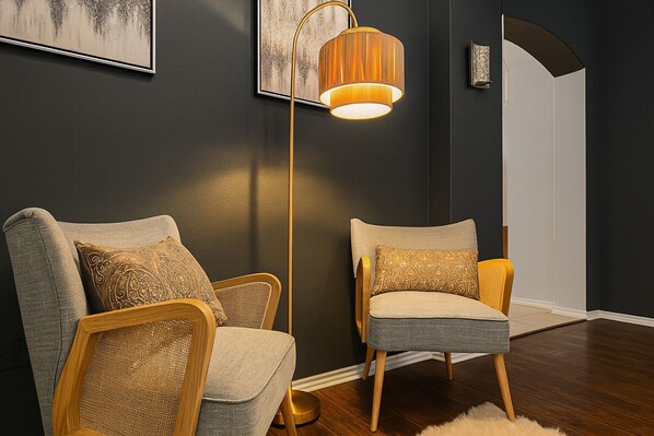 Un salon moderne avec deux fauteuils rembourrés, une lampe sur pied et une œuvre d’art encadrée accrochée au mur.