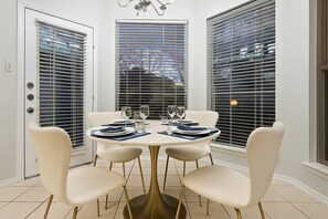 Un coin repas avec une table ronde, quatre chaises et une fenêtre avec des stores.