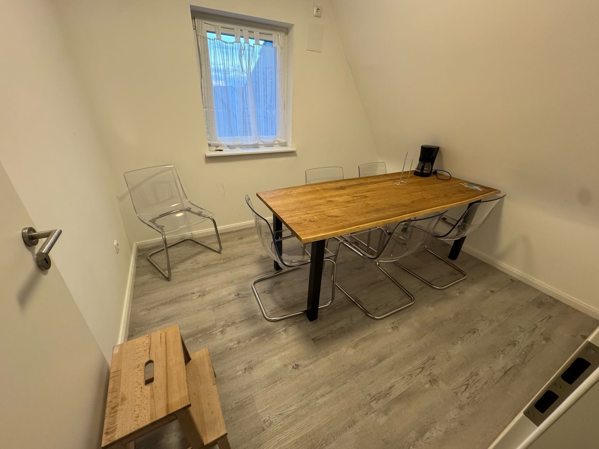 Ein Zimmer mit Holztisch und -stühlen, einem Fenster mit Vorhängen und einer Tür.