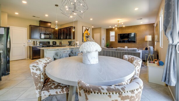 A modern kitchen with dark cabinets, a central island, and a dining area with a round table and animal print chairs. - Stylish Family Home w/ Playground in Las Vegas (Las Vegas)