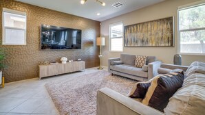 A living room with a flat-screen TV, a sofa, a coffee table, and a decorative wall. - Stylish Family Home w/ Playground in Las Vegas (Las Vegas)