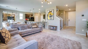 A modern living room with a sofa, a coffee table, and a rug. There is a kitchen in the background with cabinets and a refrigerator. - Stylish Family Home w/ Playground in Las Vegas (Las Vegas)