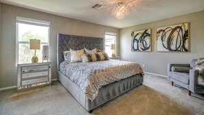 A bedroom with a large bed, a chandelier, artwork on the wall, and a view of the outdoors through the window. - Stylish Family Home w/ Playground in Las Vegas (Las Vegas)