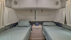 A compact interior with two beds, a small table, and a ceiling fan. - Private Catskills Campsite! Tiny Cabin + Airstream (Sidney Center)
