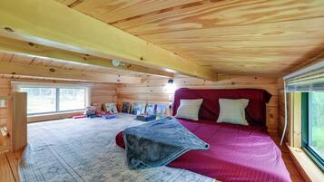 A wooden cabin interior with a bed, a rug, and a window.