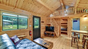 A log cabin with a sofa, television, wooden staircase, and a dining area. - Private Catskills Campsite! Tiny Cabin + Airstream (Sidney Center)