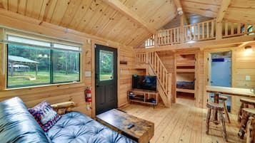 A log cabin with a sofa, television, wooden staircase, and a dining area.