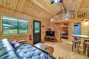 Eine Blockhütte mit einer Couch, einem Fernseher, einer Holztreppe und einem Essbereich.