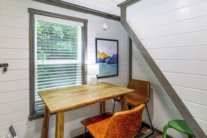 Ein Zimmer mit Holztisch, einem Stuhl, einem Fenster mit Jalousien und einem gerahmten Bild an der Wand.