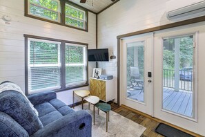 Quarto com um sofá azul, uma mesinha, uma televisão em um móvel de madeira e uma porta de vidro deslizante que dá para o exterior.