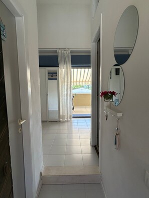 A hallway leading to a balcony with a view, a door with a handle, a mirror on the wall, and a small shelf with a vase. - Lovely 1-bedroom apartment with AC in charming Marcelli (Marcelli)