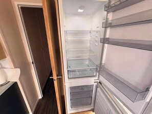 Ein Blick ins Hotelzimmer: eine Tür führt zu einem Flur, ein Bett und ein eingebauter Kühlschrank mit mehreren Ablagen.