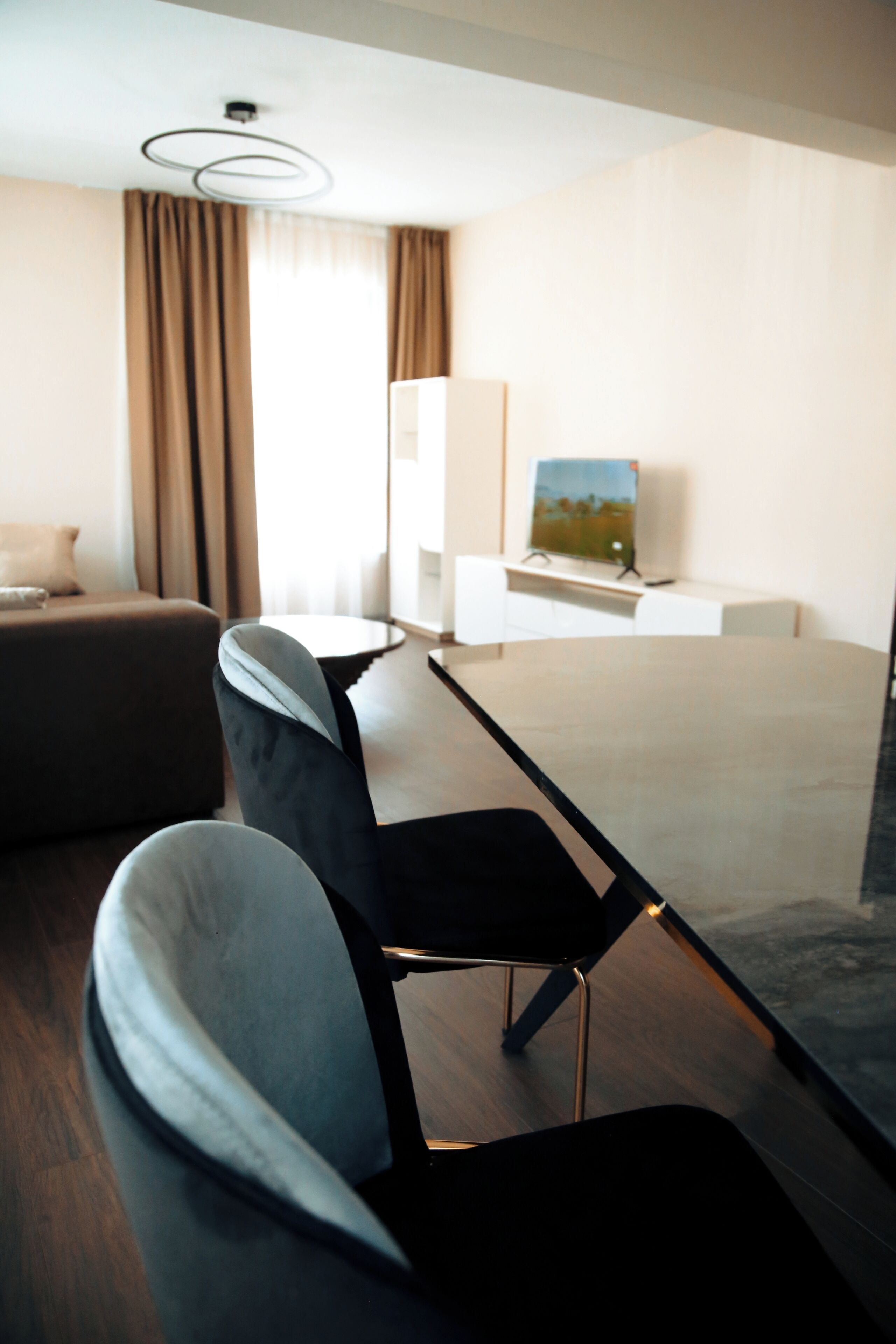A modern hotel room with a bed, a desk, a chair, a television, and a window with curtains.