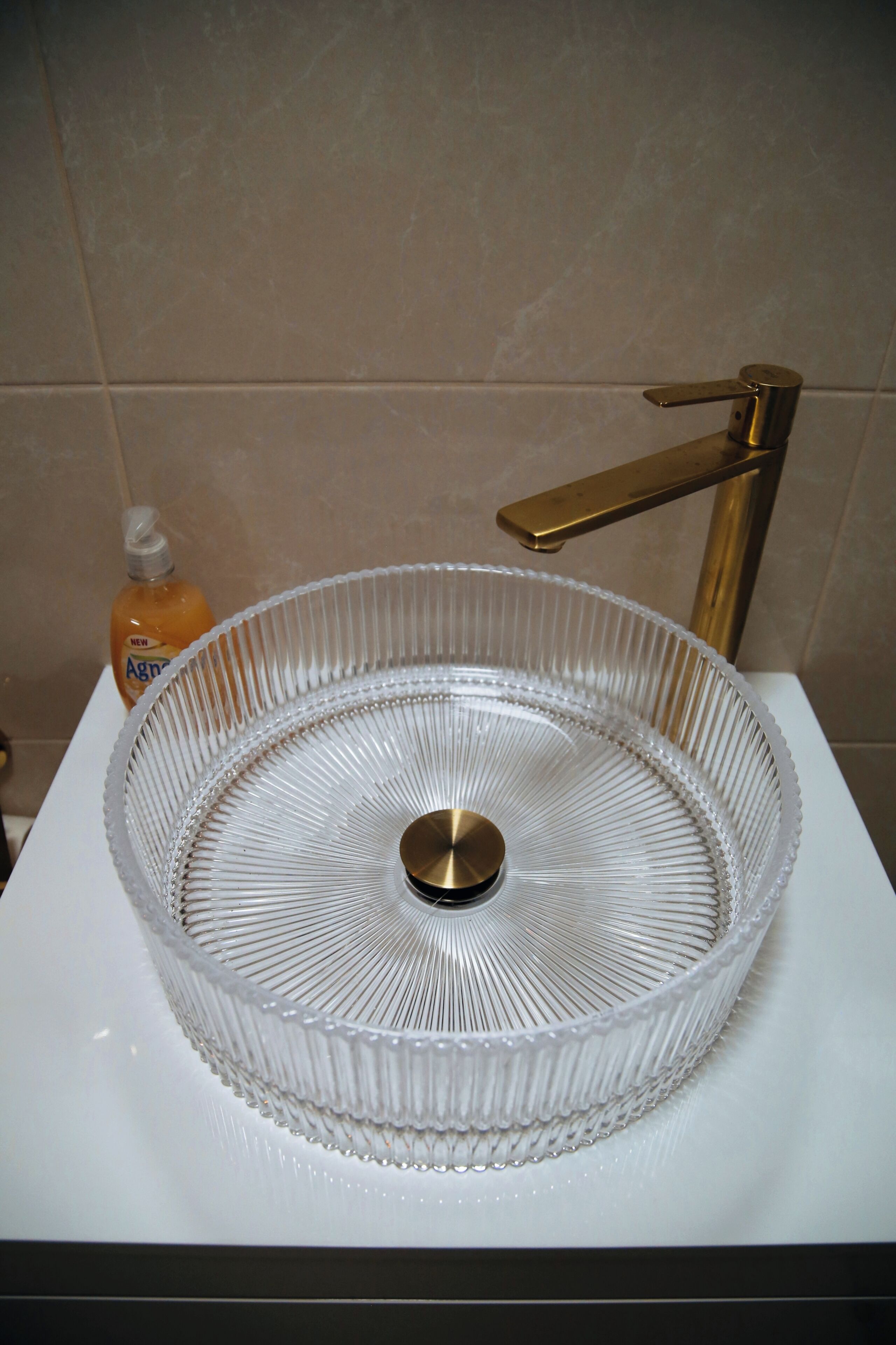 Une salle de bain avec un lavabo en verre et un robinet doré.