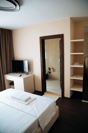 Habitación de hotel con cama, escritorio con televisor, baño visible a través de una puerta abierta y armario.