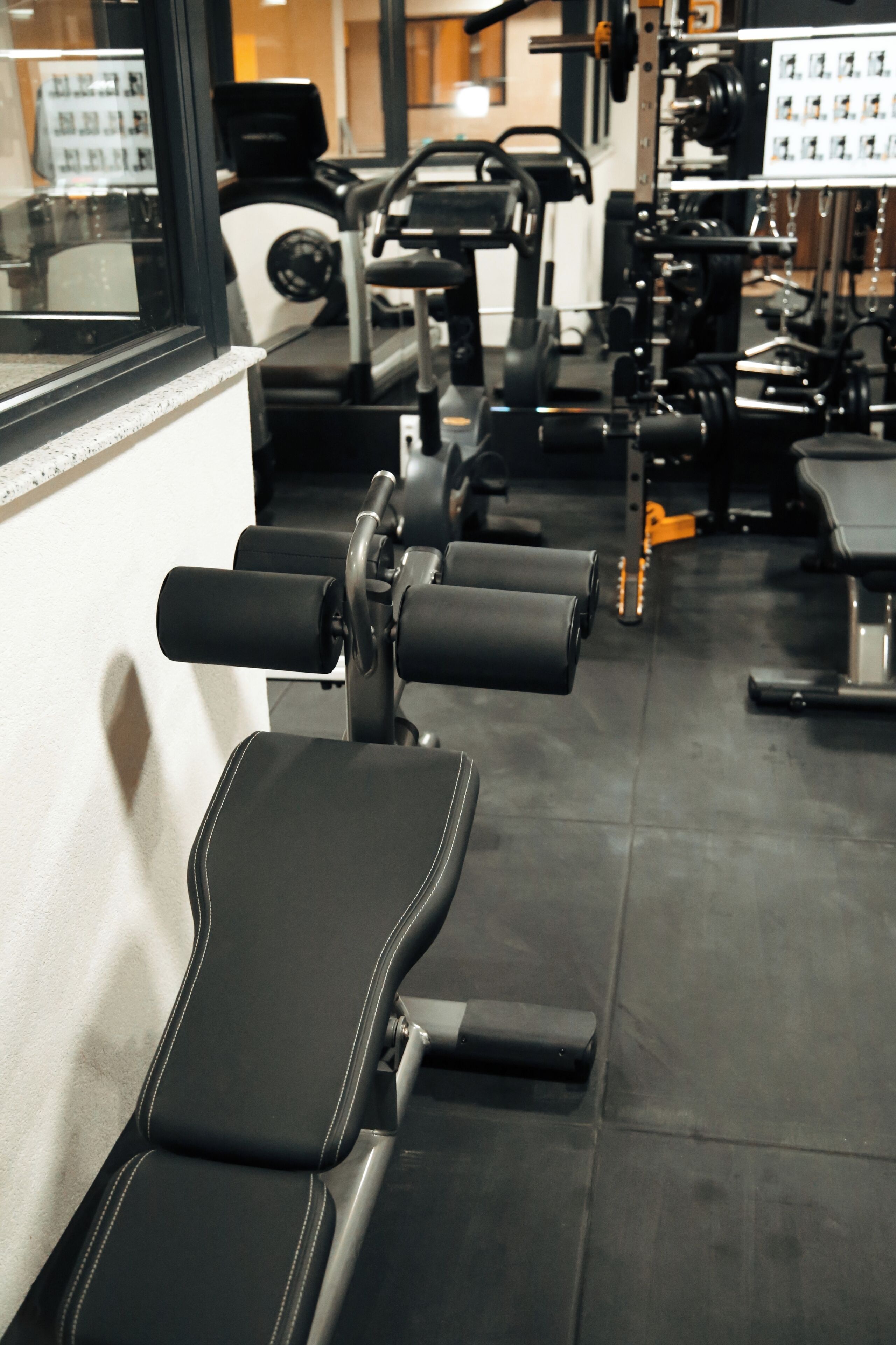 A row of black exercise benches in a gym with various fitness equipment in the background.
