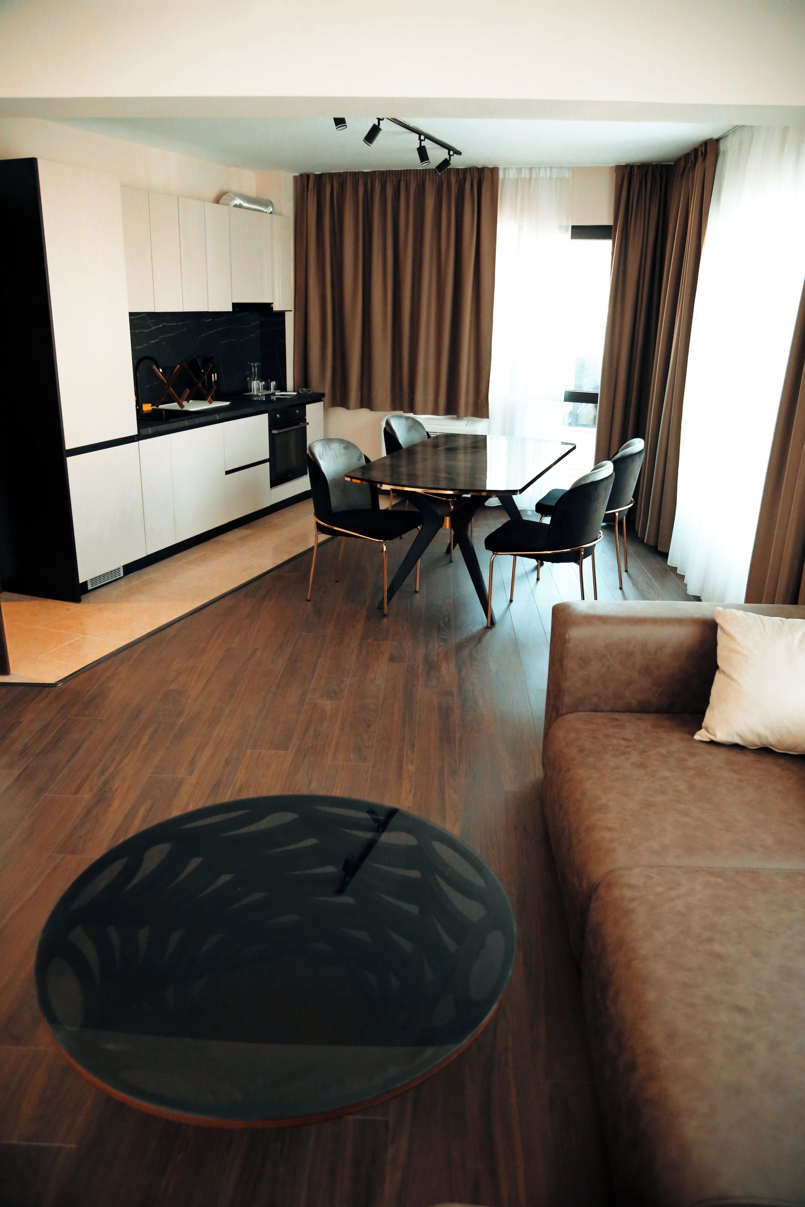 A modern living room with a brown sofa, a round coffee table, and a dining area with a table and chairs.