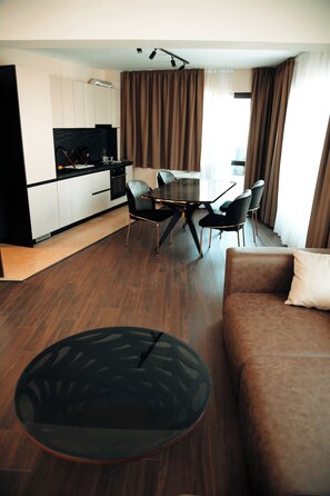 A modern living room with a brown sofa, a round coffee table, and a dining area with a table and chairs.