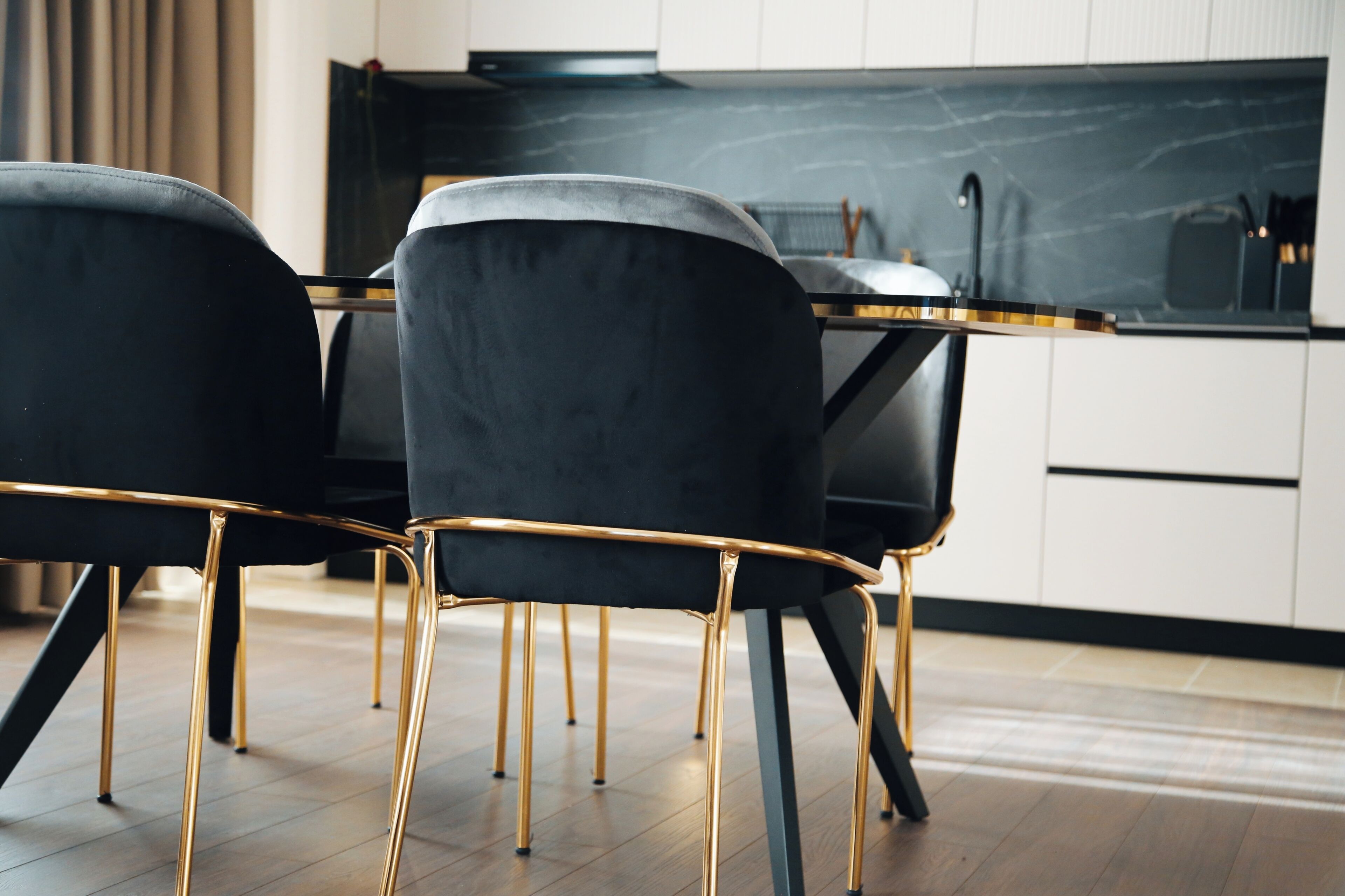A modern kitchen with black chairs and gold legs, a black countertop, and white cabinets.
