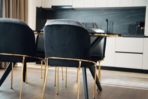 A modern kitchen with black chairs and gold legs, a black countertop, and white cabinets.