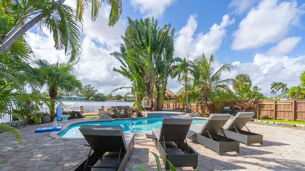 A swimming pool with lounge chairs, palm trees, and a view of the water. - Waterfront Jungle Home with Kayaks (Miami)
