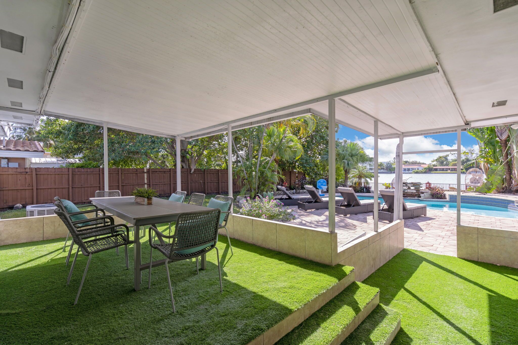 Un patio couvert avec une piscine, du mobilier d’extérieur et une vue sur l’eau.