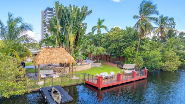 Un resort junto al río con una estructura de techo de paja, una terraza roja con asientos y abundante vegetación tropical.