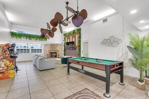 Ein Freizeitraum mit Billardtisch, Deckenventilator, einer Couch und einem Fernseher.