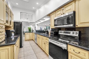 A modern kitchen with beige cabinetry, a black countertop, stainless steel appliances, and a tiled floor. - Waterfront Jungle Home with Kayaks (Miami)