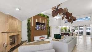 Un amplio espacio de estar con chimenea, televisor de pantalla plana y un ventilador moderno en el techo.