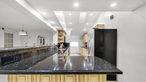 A modern kitchen with a large granite island, stainless steel appliances, and light wood cabinetry. - Waterfront Jungle Home with Kayaks (Miami)