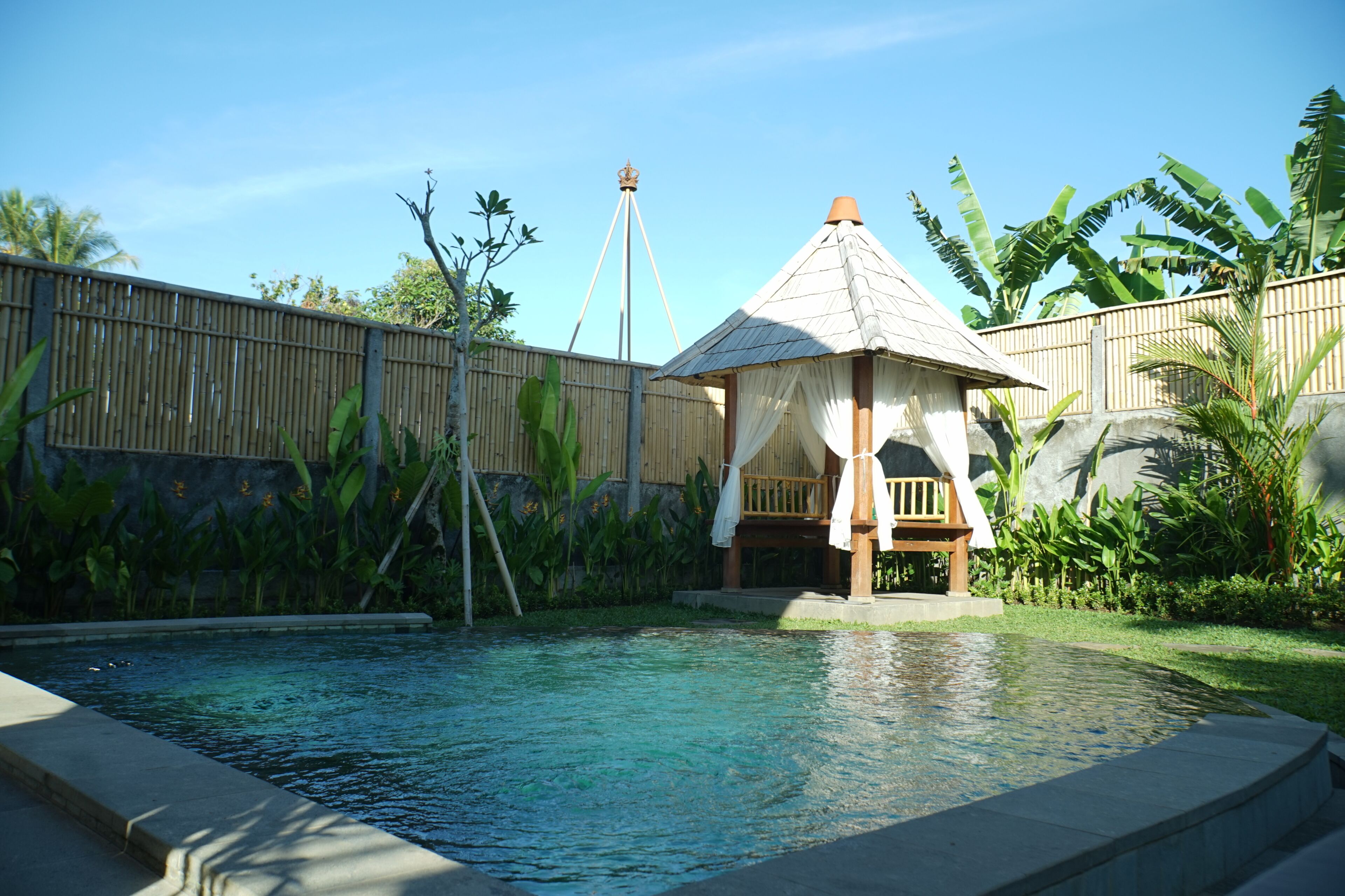 A pool area with a small gazebo and a bamboo fence.