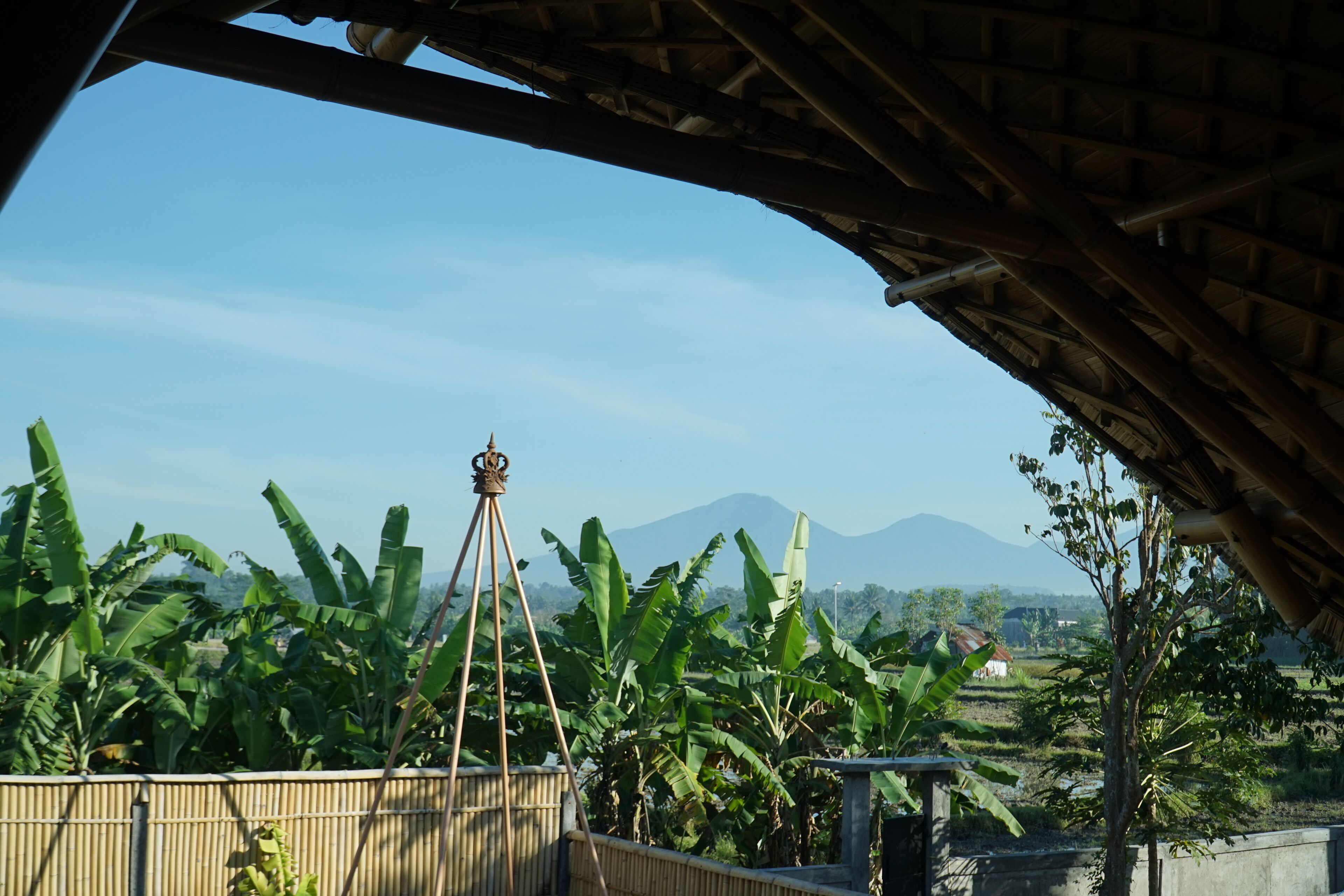 Blick von einer überdachten Terrasse mit Bambuszaun, einem Stativ und einem Berg im Hintergrund.