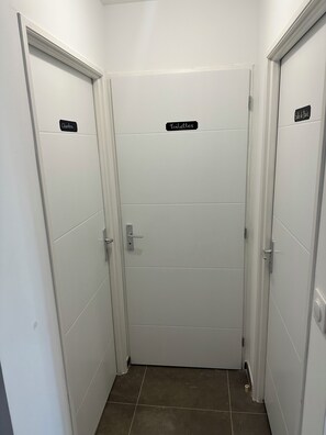 A hallway with two doors, one labeled 'Chambre' and the other 'Toilettes,' leading to a bathroom. - T2 in the heart of Suze - Between Vineyards and History (Suze-la-Rousse)