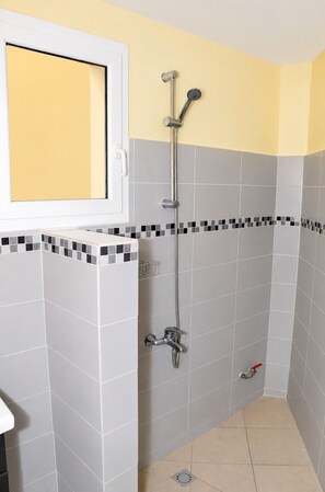 Un baño con ducha, paredes de azulejos y una ventana.