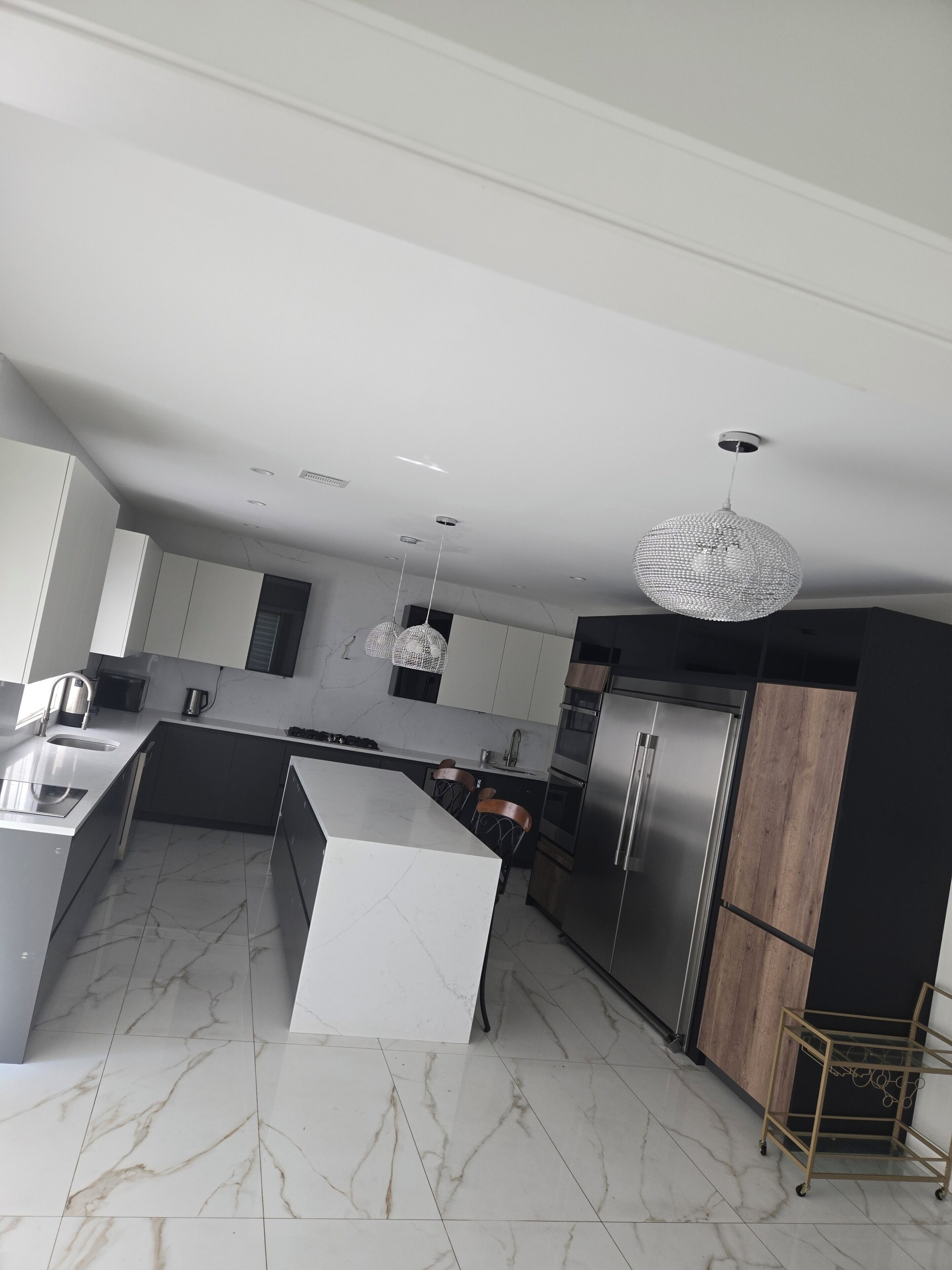 A modern kitchen with a marble floor, stainless steel appliances, and pendant lighting.