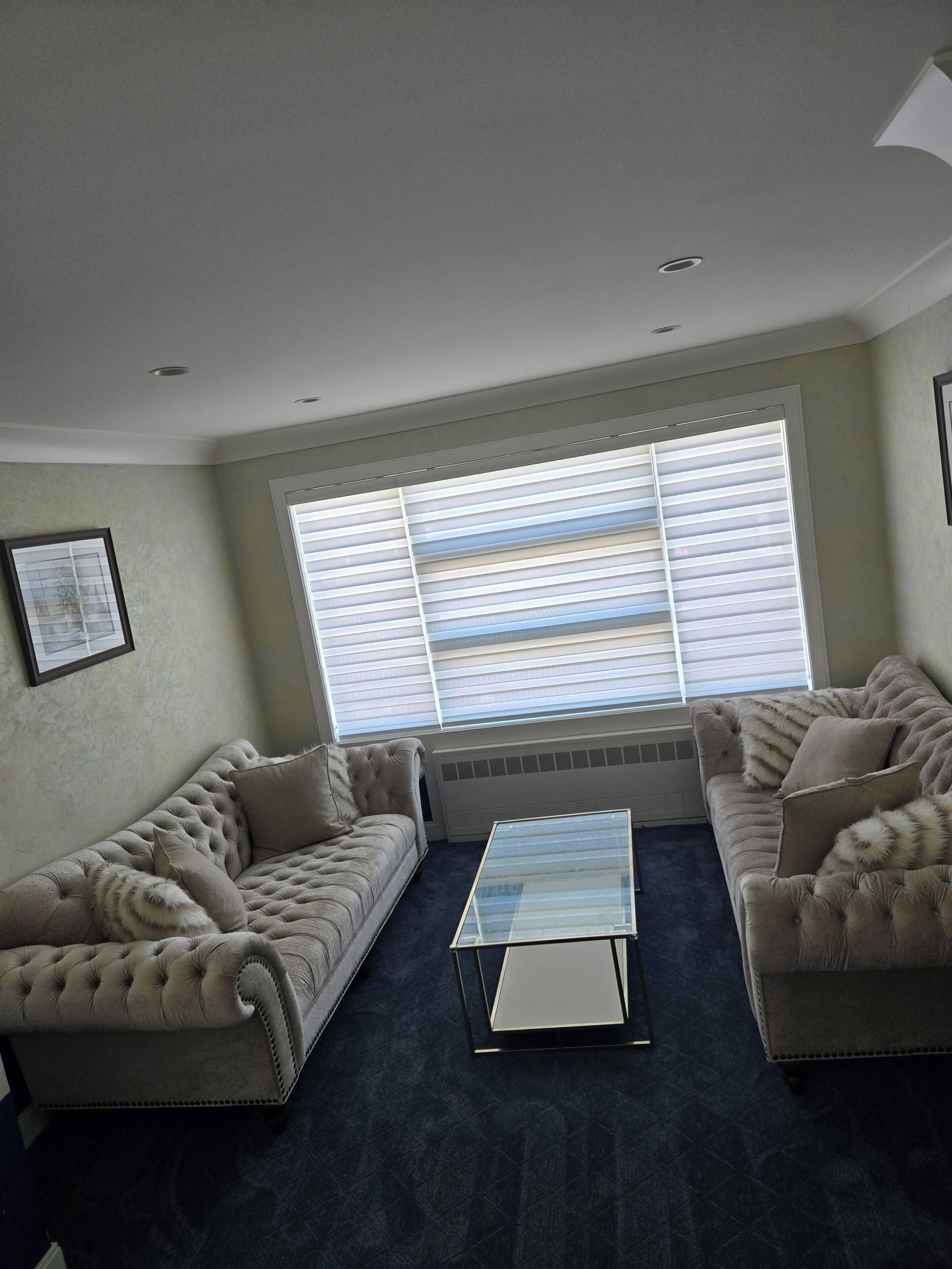 A living room with two sofas, a glass coffee table, and a large window with blinds.