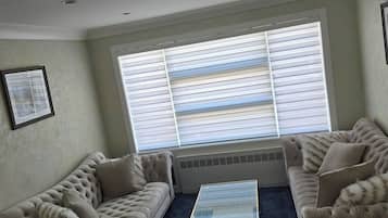 A living room with two sofas, a glass coffee table, and a large window with blinds.