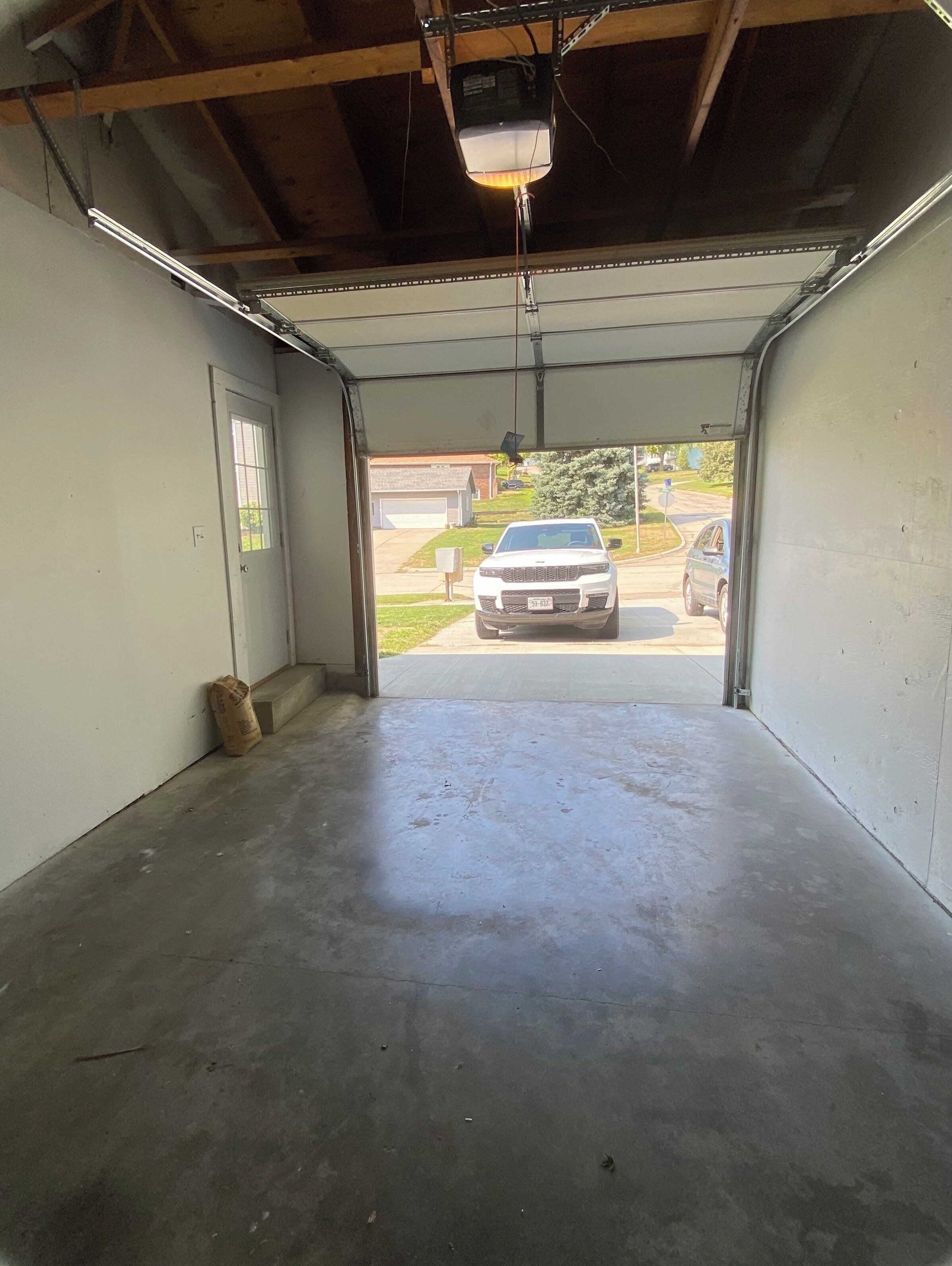 An empty garage with a concrete floor and a white car parked outside.