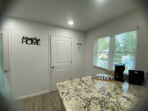 A kitchen with a granite countertop, a coffee maker, and a window with blinds.