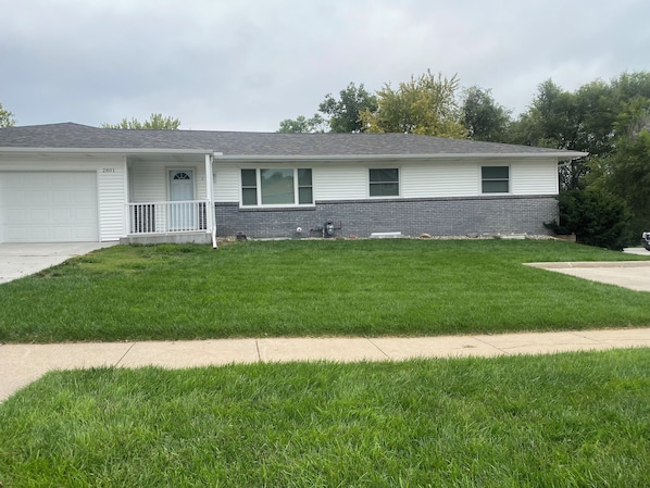 A two-story residential building with a garage, a front porch, and a well-maintained lawn.