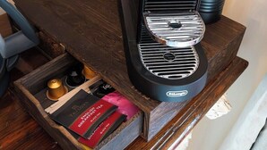 Une machine à café posée sur une surface en bois, avec un tiroir contenant des sachets de thé.