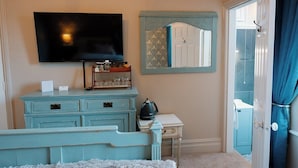 Une pièce avec un téléviseur fixé au mur, une commode avec des tiroirs, une petite table avec une bouilloire et une porte donnant sur une autre pièce.