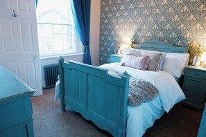 Quarto com cama verde-água, roupa de cama branca e papel de parede estampado.