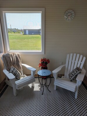 Une pièce comprenant deux fauteuils Adirondack blancs, une petite table ronde dont le plateau est orné d’un motif bleu, et un pot de fleurs avec des fleurs rouges.