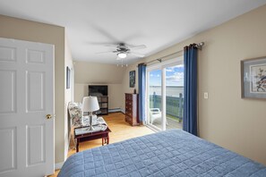 A bedroom with a bed, a television, a chair, a dresser, and a balcony with a view.